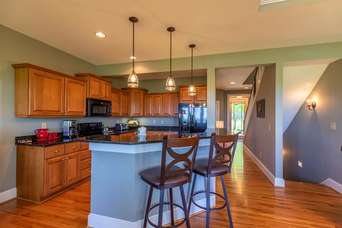 A welcoming kitchen with a large island, wooden cabinets, pendant lights, and bar stools, creating an ideal spot for cooking and casual conversations. The warm tones and inviting setup highlight the kitchen as a social hub.