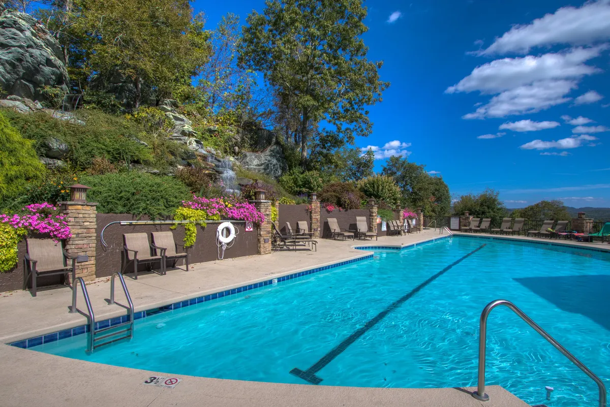 An exterior shot of a sparkling swimming pool surrounded by lounge chairs, flower beds, and natural rock formations. The relaxed atmosphere suggests both fun family moments and tranquil relaxation, with the pool area inviting guests of all ages to unwind or play.