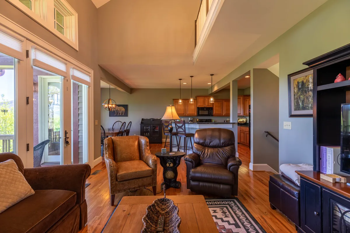 An open living area with plush seating facing a kitchen island, framed by large windows and a decorative lamp. The setup highlights the seamless flow between living and kitchen spaces, perfect for social gatherings and shared activities.