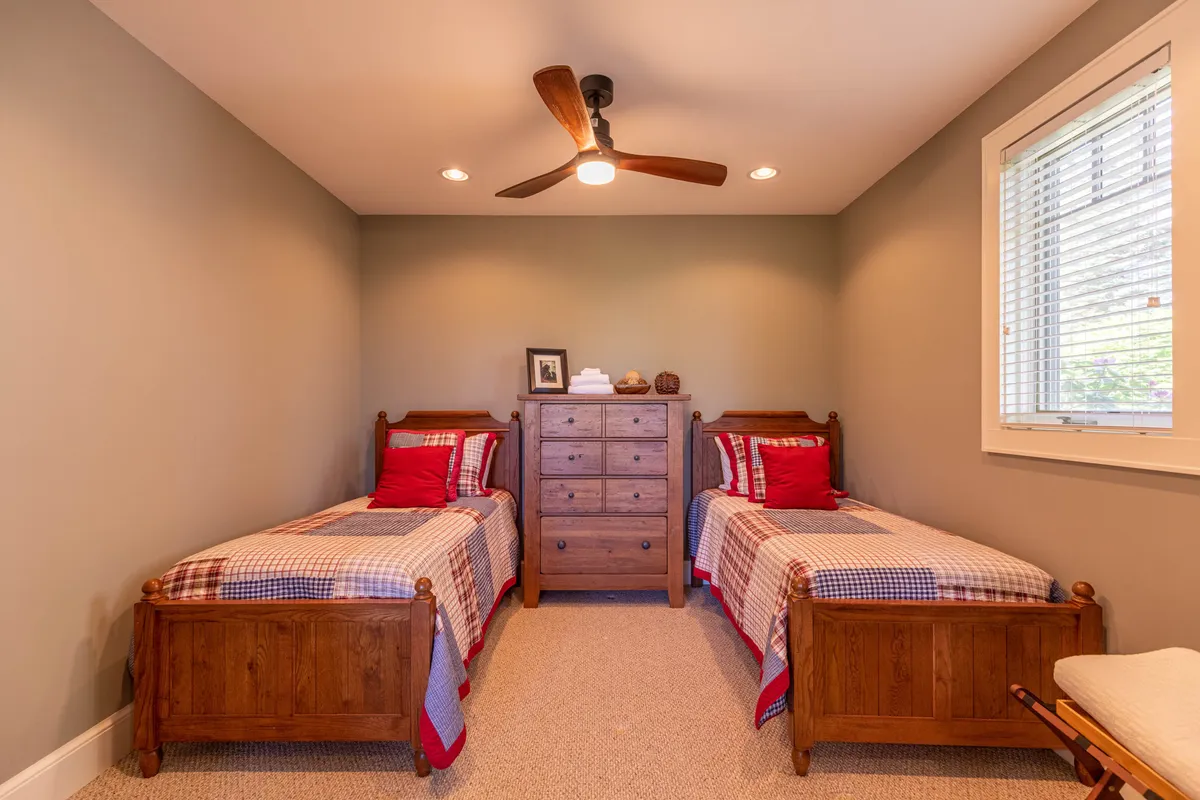 A warm, inviting bedroom with two wooden beds, a chest of drawers, and charming decorative items atop the dresser. The room is designed for sharing and togetherness, with a homey touch that makes it ideal for kids, teens, or siblings.