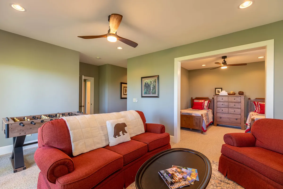 A casual game room space with a red sofa, foosball table, wall artwork, and a visible bedroom area, suggesting a multifunctional zone for both entertainment and extra sleeping accommodations.