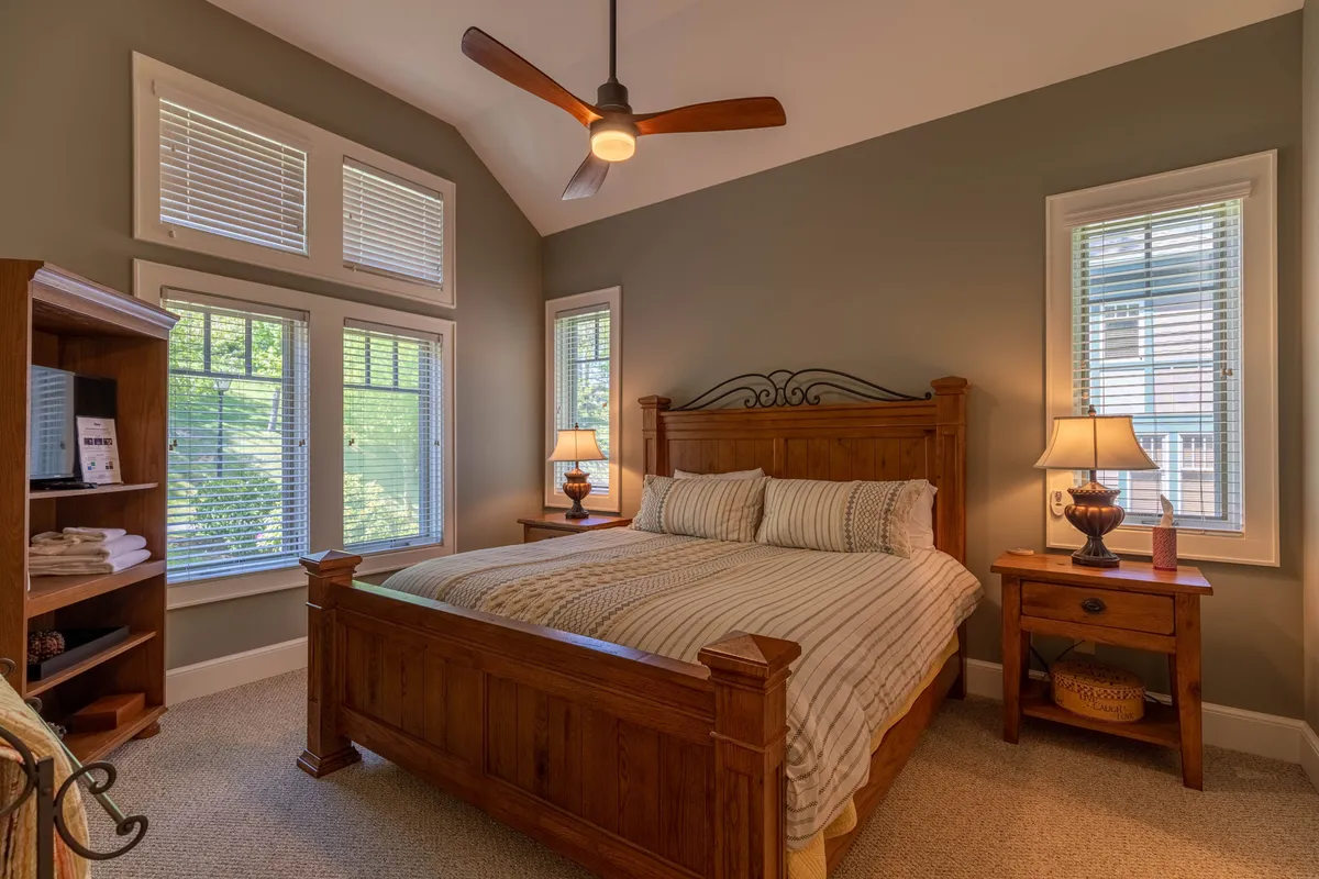 A cozy bedroom featuring a comfortable bed with plush pillows, nightstands with lamps, windows allowing in natural light, and a bookshelf for evening reading. The space is designed for relaxation and quiet moments, evoking a sense of privacy and comfort.