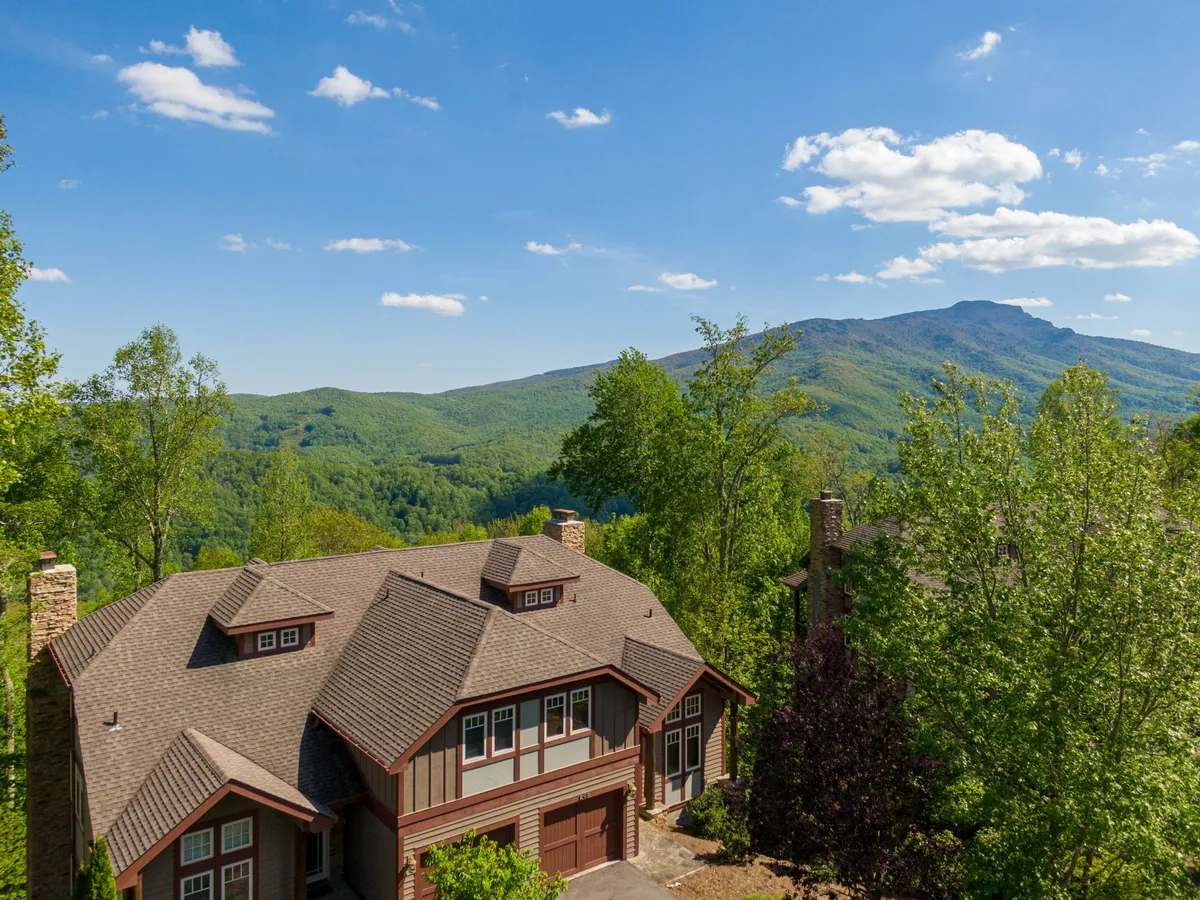 The image displays the exterior of a spacious condo nestled among tall trees, with a sweeping mountain range in the background. The porch offers an inviting spot to take in breathtaking sunrises, and the setting exudes tranquility, perfect for relaxing or enjoying outdoor activities like hiking and stargazing.