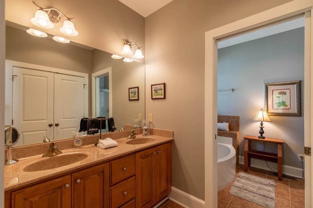A bright, tranquil bathroom with a double sink vanity, framed artwork, and a bathtub—projecting luxury and ample space for self-care and morning routines.